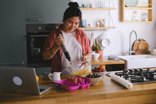 Woman using a mixer in a modern kitchen, preparing food with fresh ingredients.